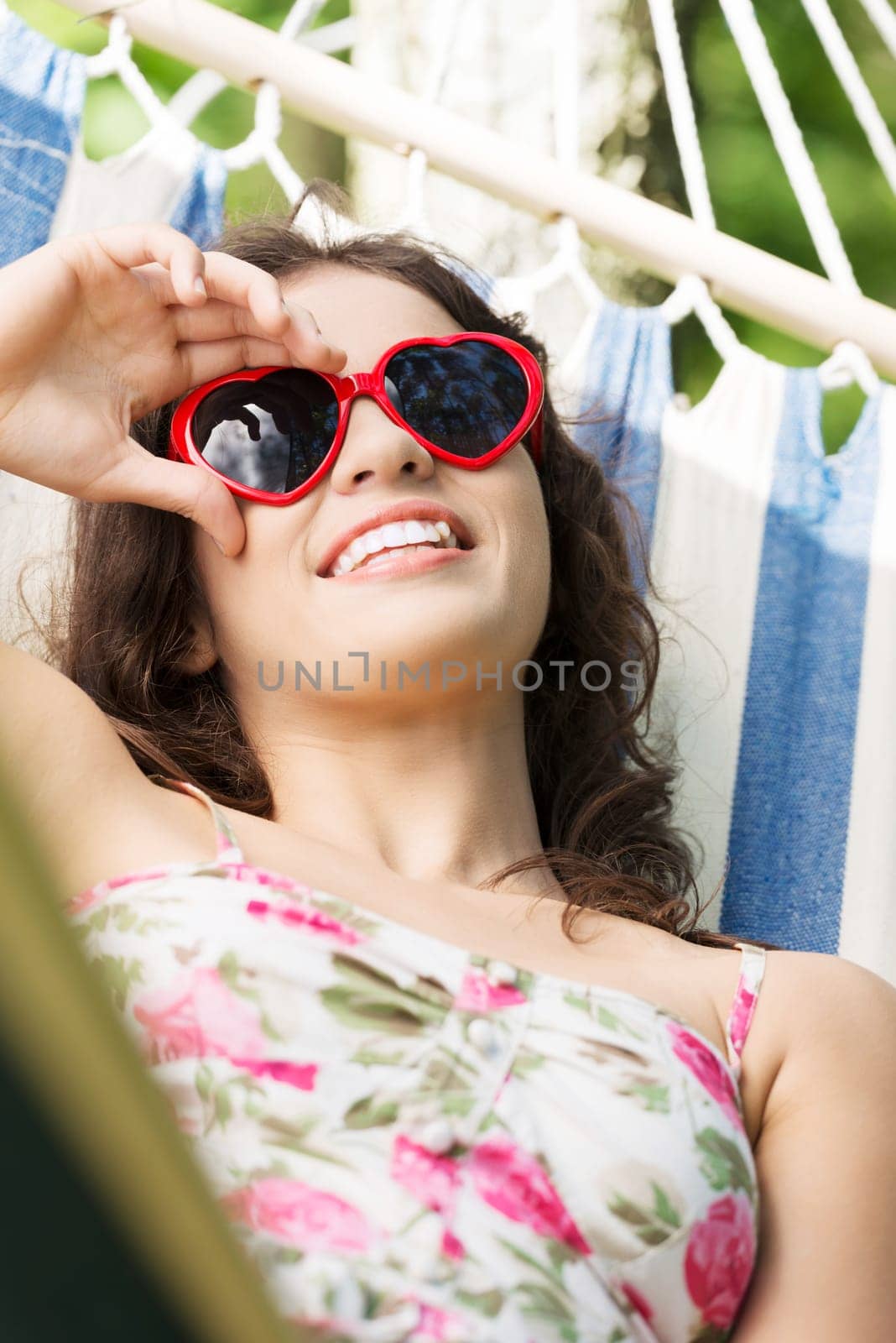 Young woman lying in a hammock in garden with heart shaped sunglasses.