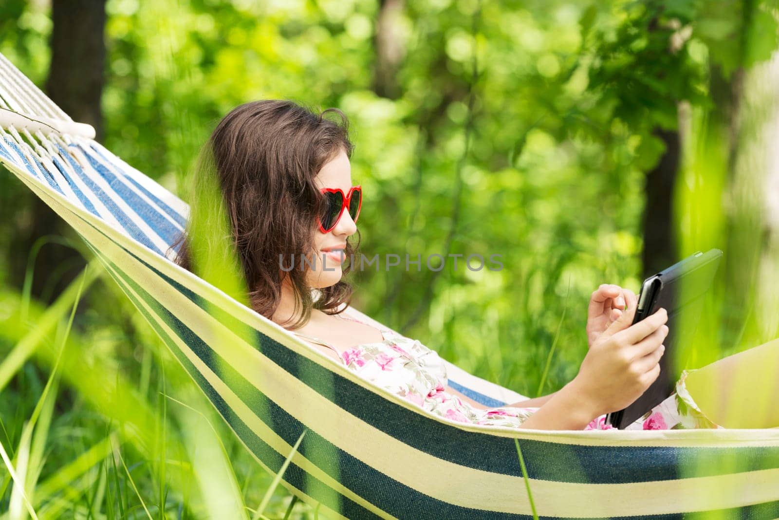 young woman lying in a hammock in the garden with e-book on tablet computer.