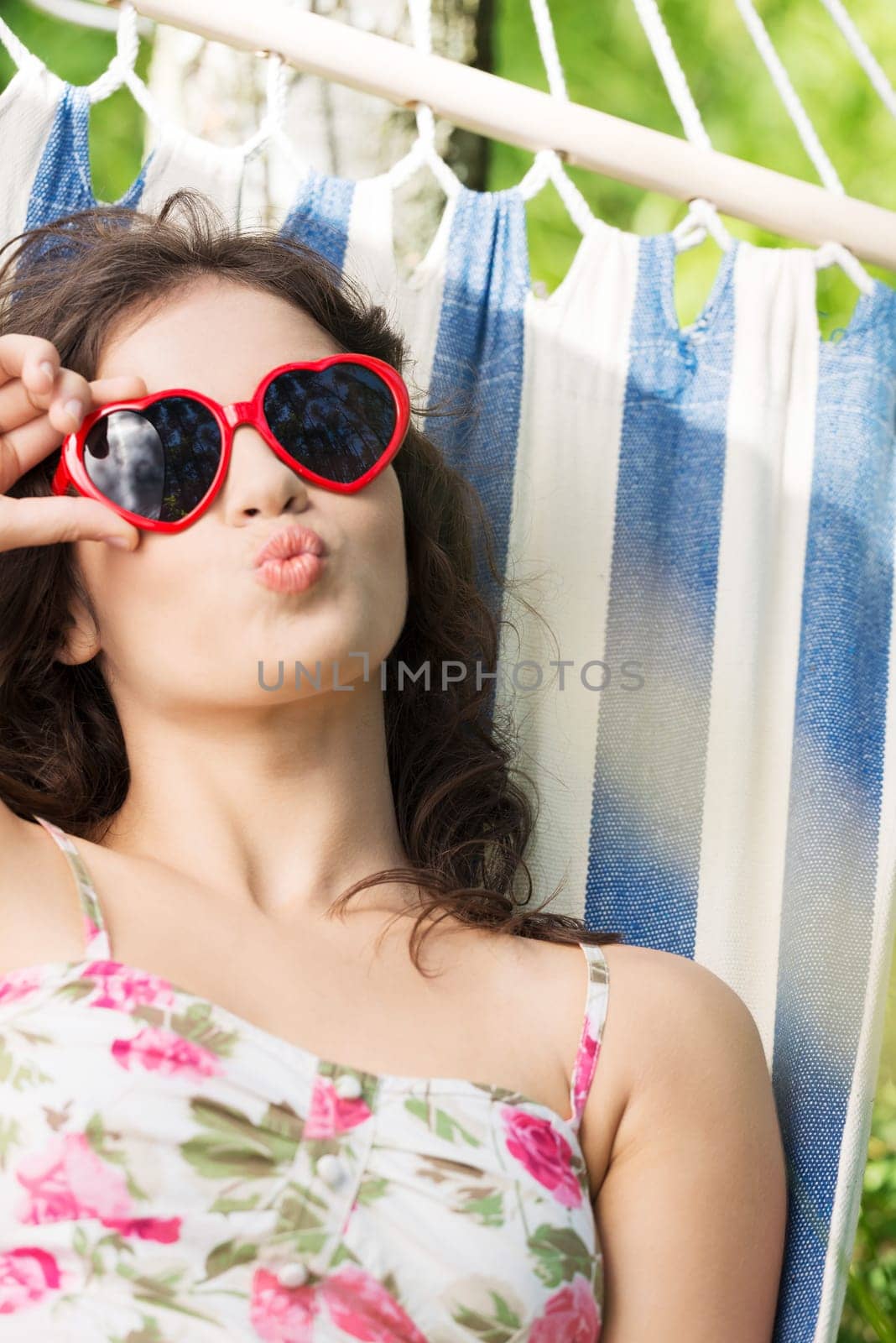 young woman lying in a hammock in the garden with heart shaped sunglasses.