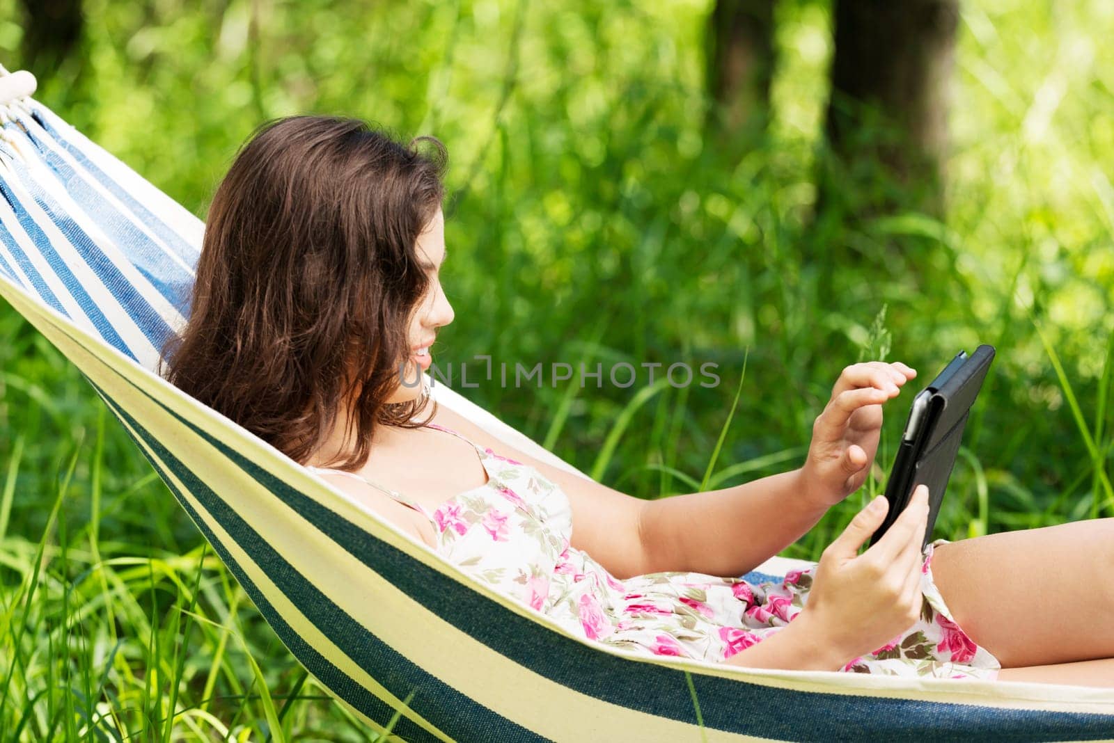 young woman lying in a hammock in the garden with e-book on tablet computer.