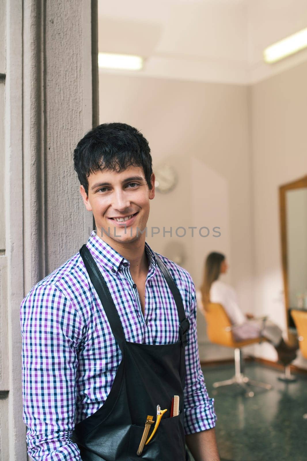 portrait of young male hairstylist standing out of shop and looking at camera