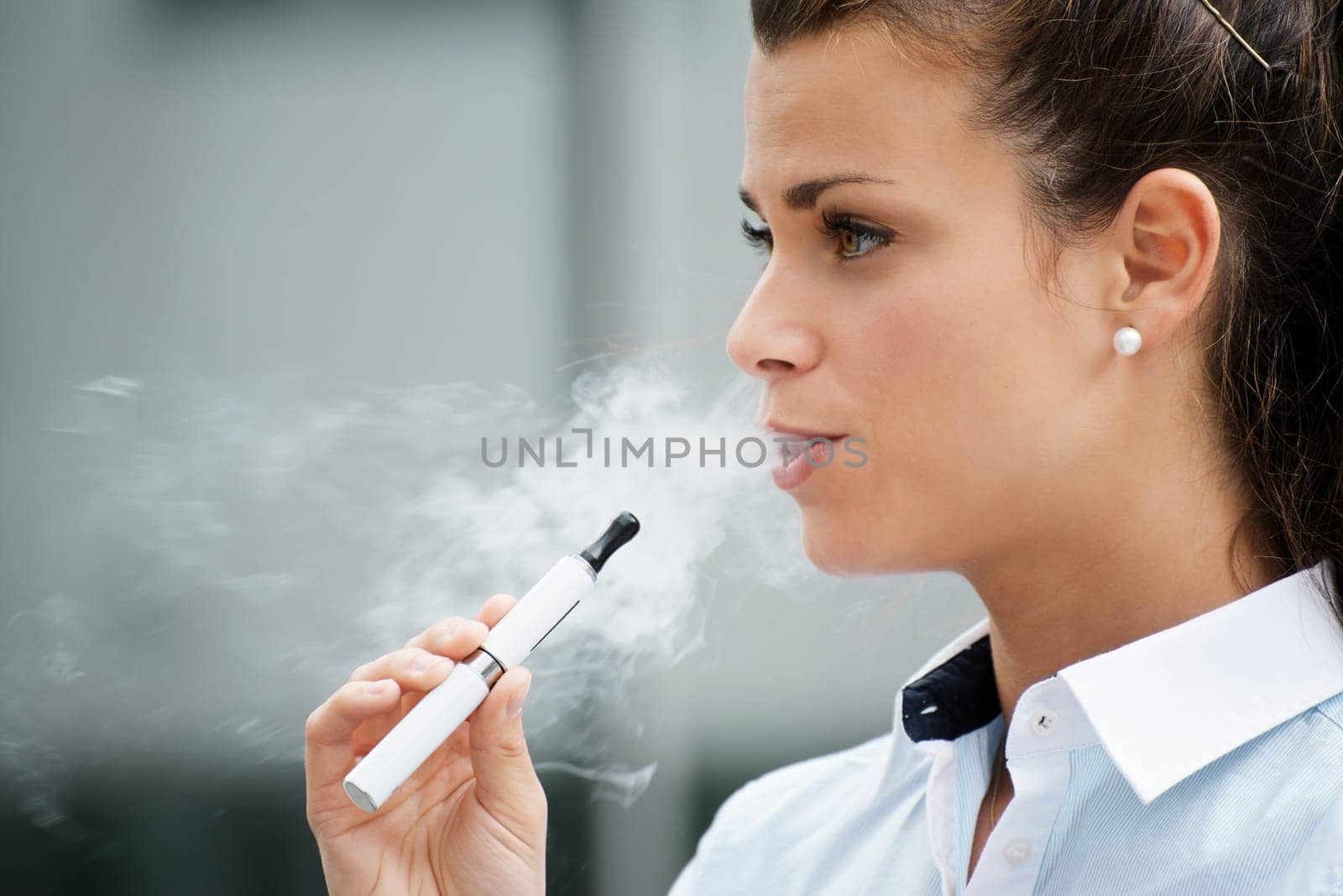 young female smoker smoking e-cigarette outdoors. Head and shoulders, side view
