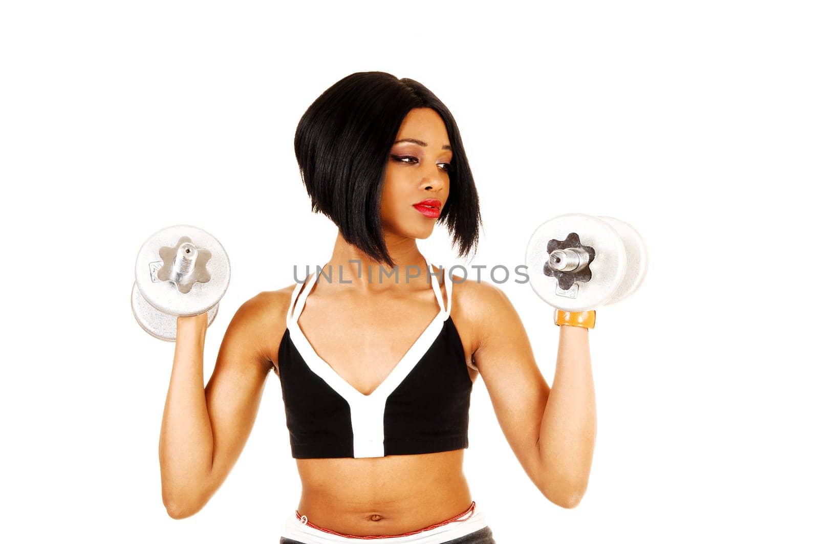 A slim young woman in black exercise clothing working out with silver.color dumbbells for white background..