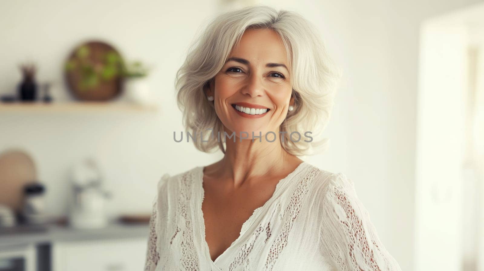 Portrait of beautiful happy smiling mature woman looking at camera standing in white room at home, toothy smile