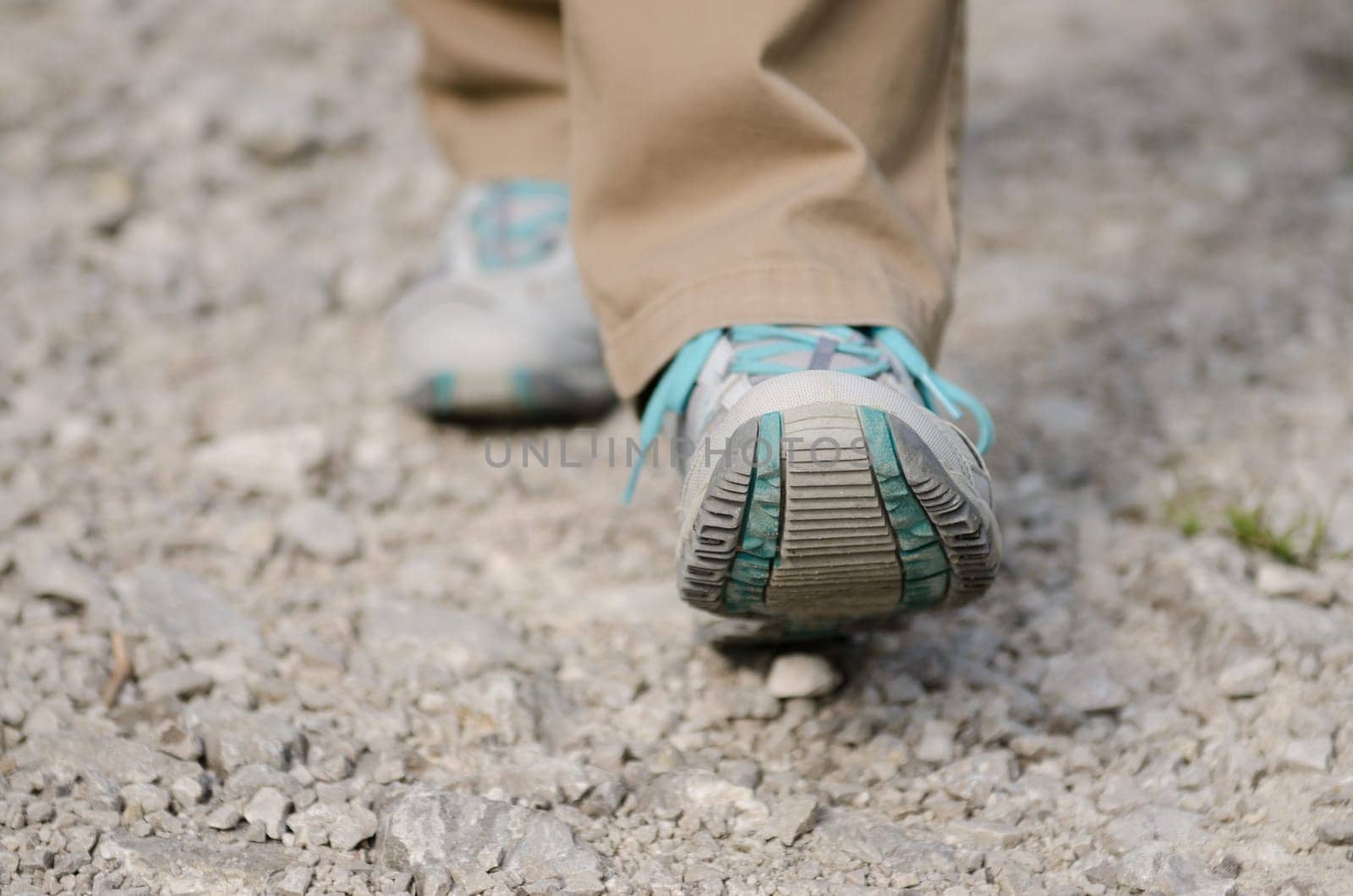 Close-up of two feet with shoes walking on a path with stones
