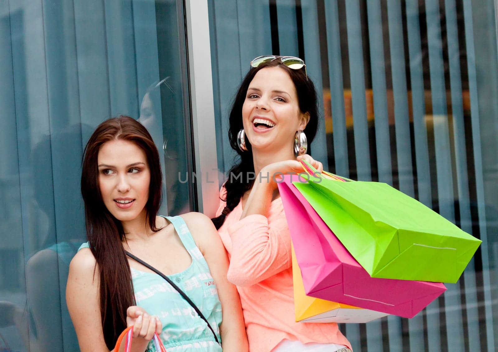 Two young laughing women shopping with colourful shopping bags in summer
