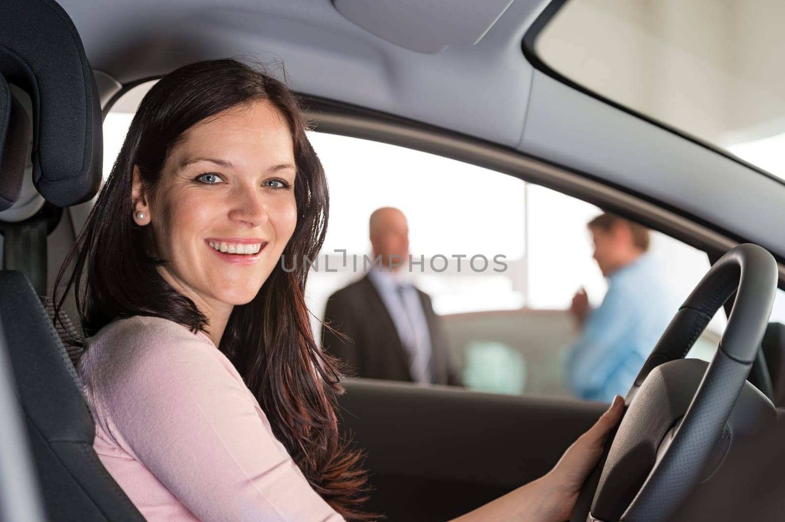 Portrait of smiling woman sitting in car in showroom