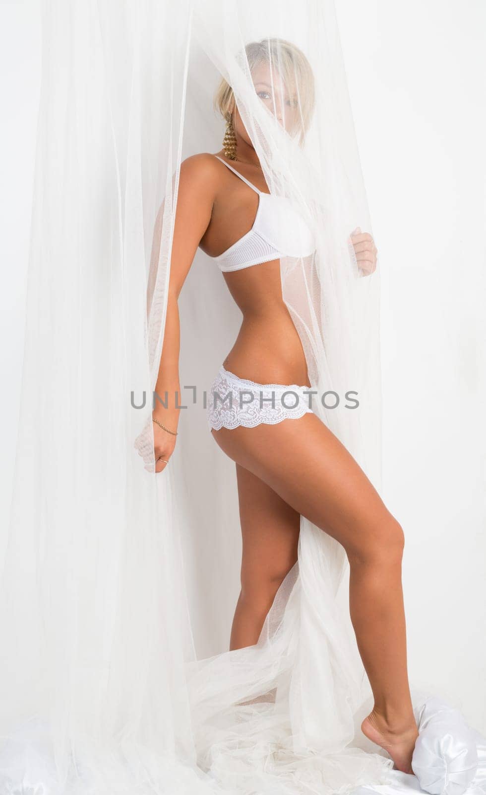 Tanned girl in lingerie on the bed under the veil.
