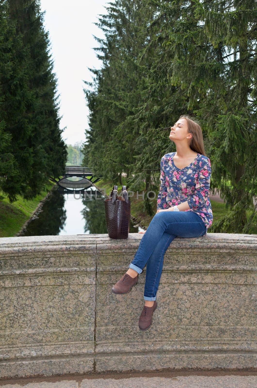 eautiful girl sits on an old stone bridge in the coniferous forest