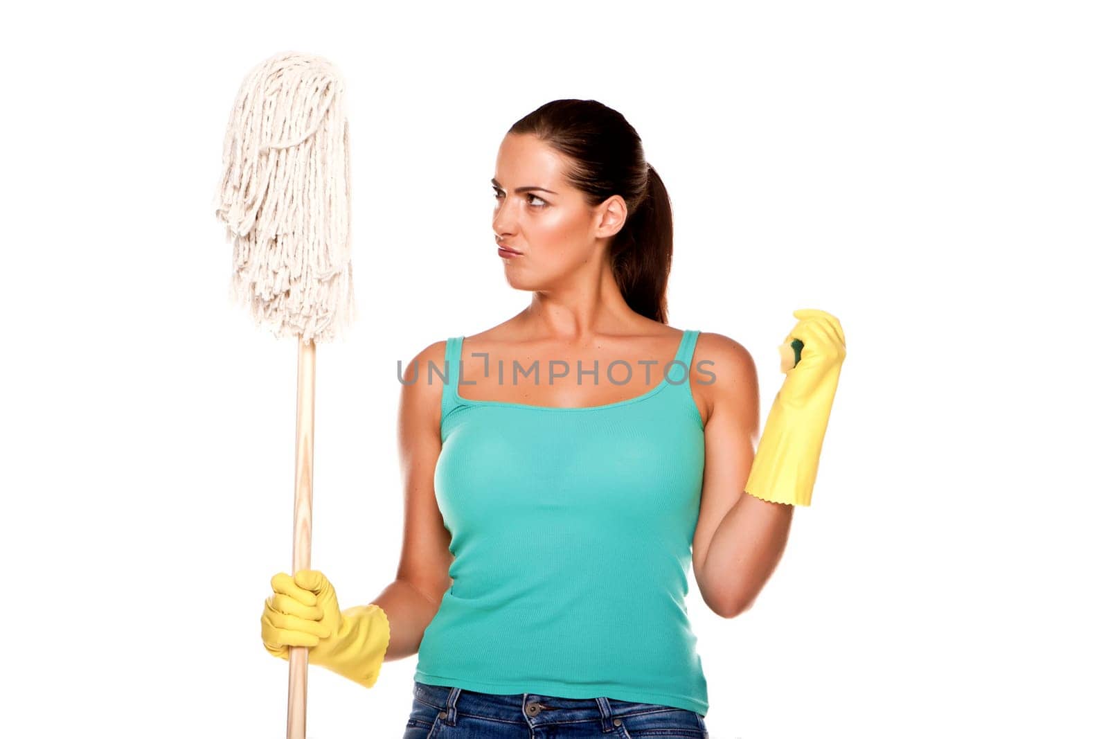 An attractive young woman with brunet hair wearing a blue vest top and yellow rubber cleaning gloves and doing some cleaning on a white background .