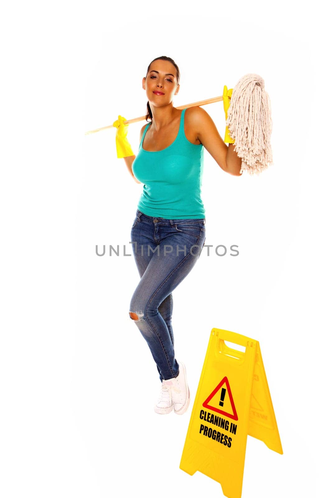 An attractive young woman with brunet hair wearing a blue vest top and yellow rubber cleaning gloves and doing some cleaning on a white background .