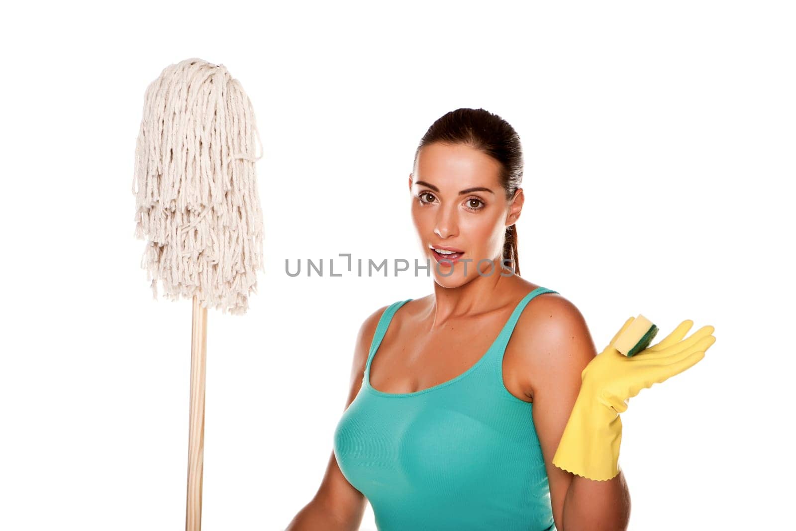 An attractive young woman with brunet hair wearing a blue vest top and yellow rubber cleaning gloves and doing some cleaning on a white background .