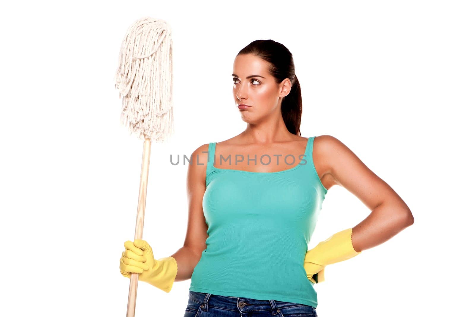 An attractive young woman with brunet hair wearing a blue vest top and yellow rubber cleaning gloves and doing some cleaning on a white background .