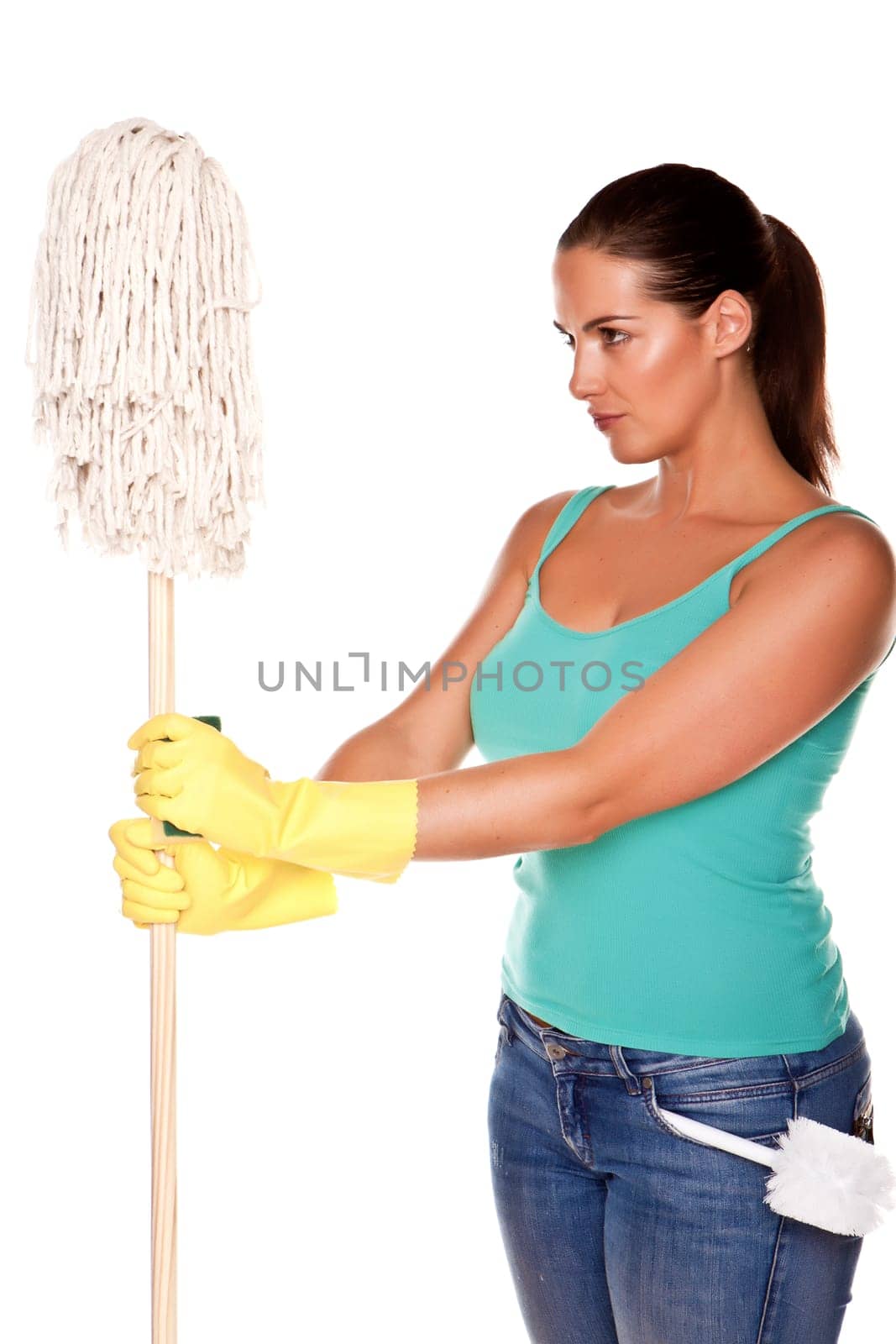 An attractive young woman with brunet hair wearing a blue vest top and yellow rubber cleaning gloves and doing some cleaning on a white background .