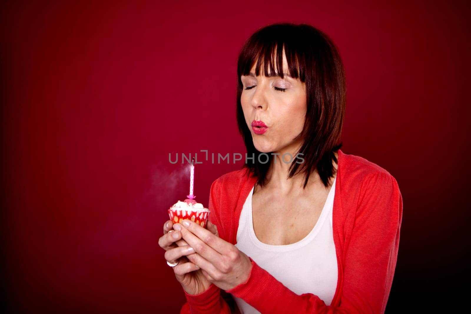 A beautiful woman is blowing out a candle on a cupcake and making a wish for her birthday.