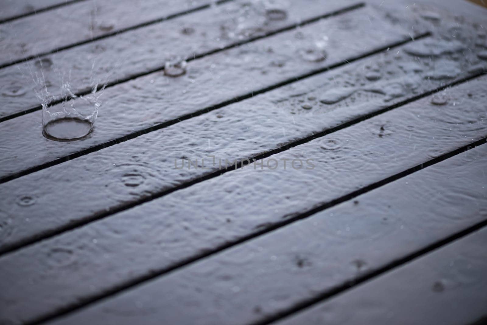 Splashing rain water droplets pattern on wooden table close-up