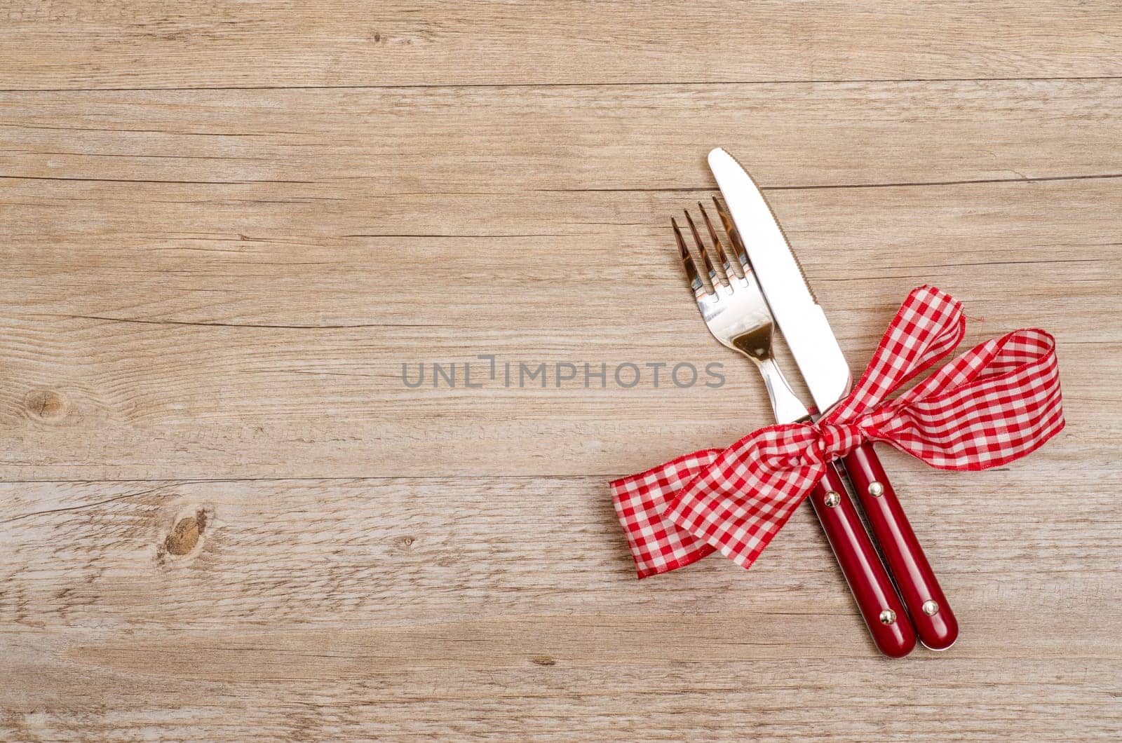 Rustic wooden table with knife and fork in red as a menu