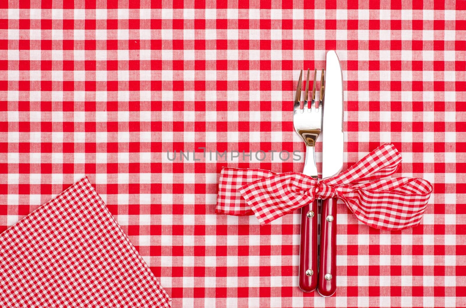 Knife and fork with bow and napkin on red checkered cloth from a dining table