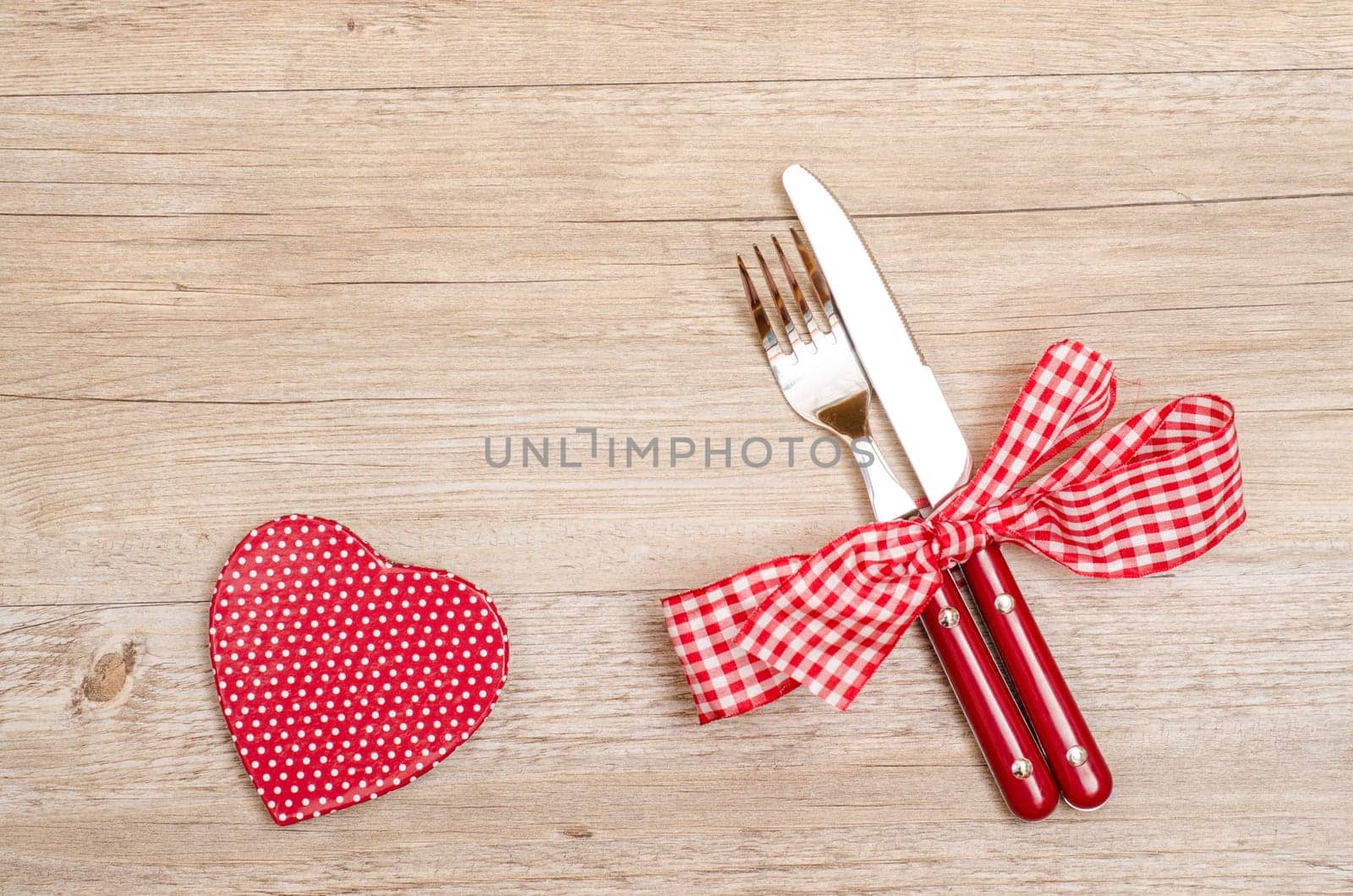 Knife and fork and red heart with white dots on a wooden table