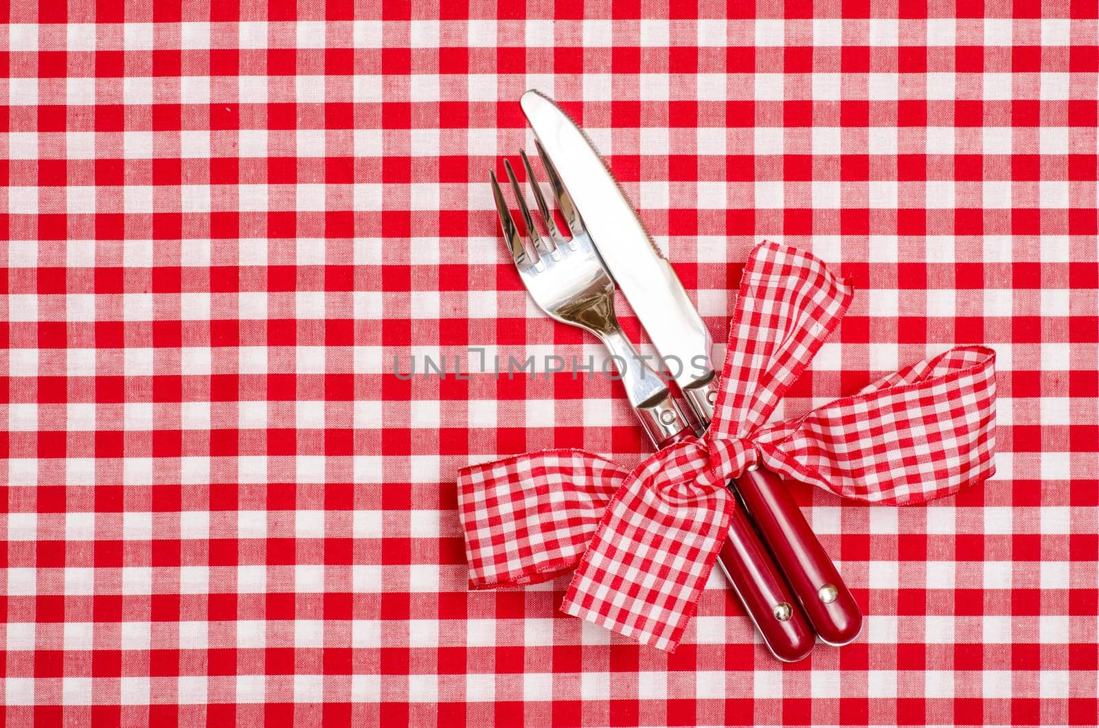 Knife and fork with red checkered bow on a tablecloth