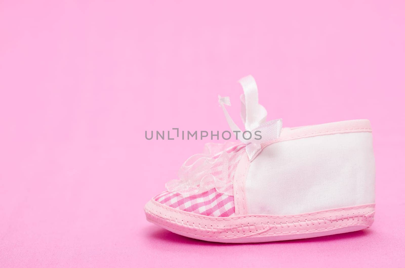 Female baby shoe with bow on pink background