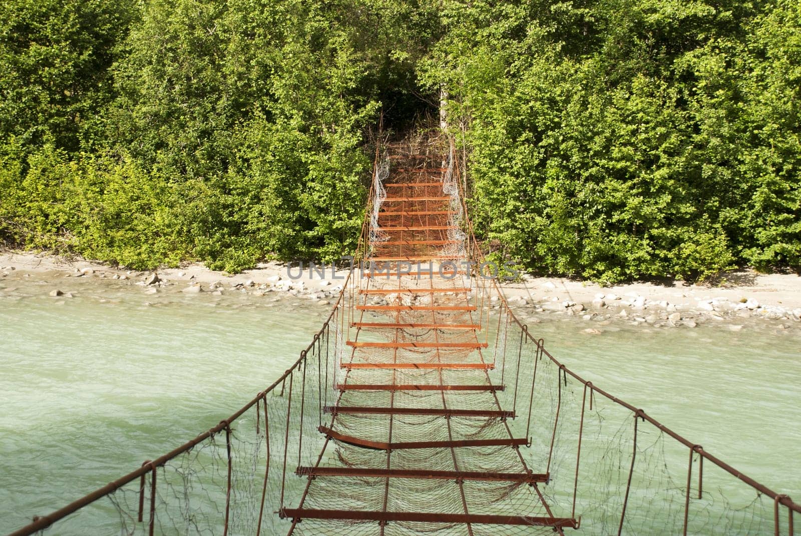 A Rusty Dangerous Bridge Leads over a Turquois River into the Woods