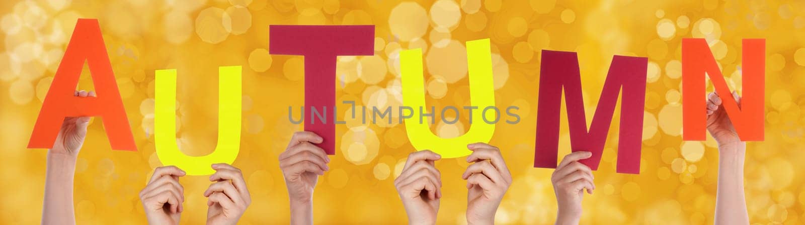 Many Hands Holding the Word Autumn with a Yellow Background
