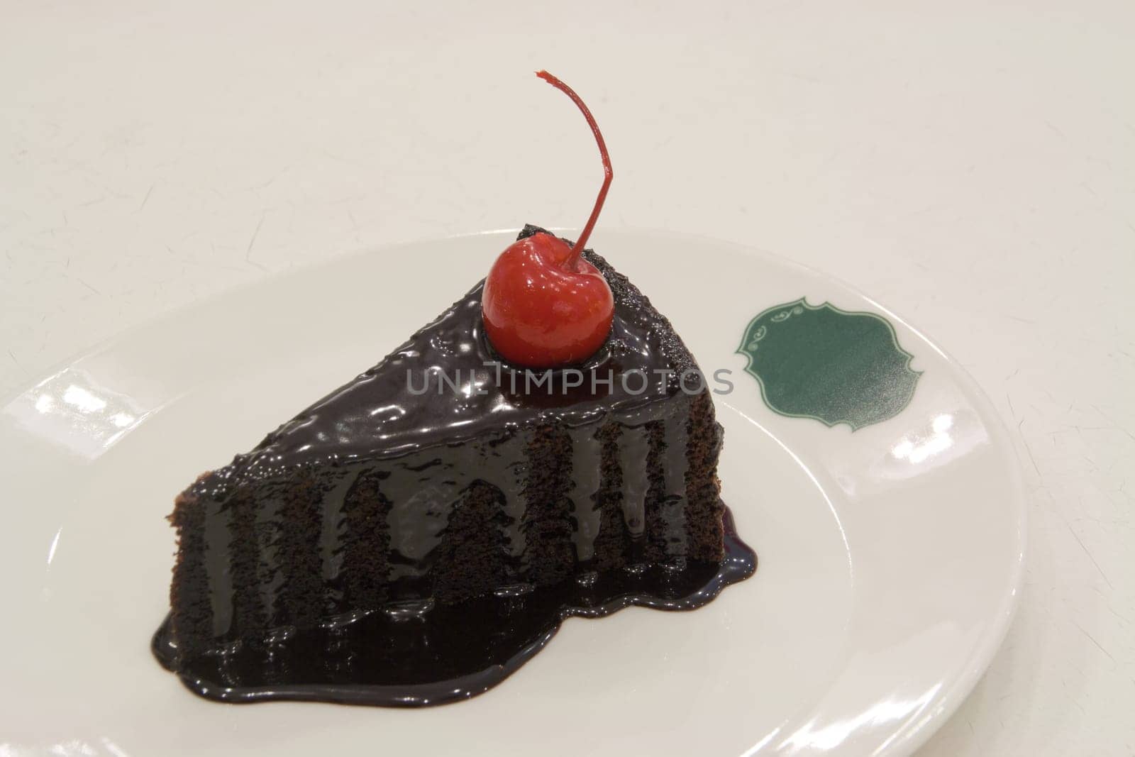 Chocolate cake decorated with red cherries on white plate.