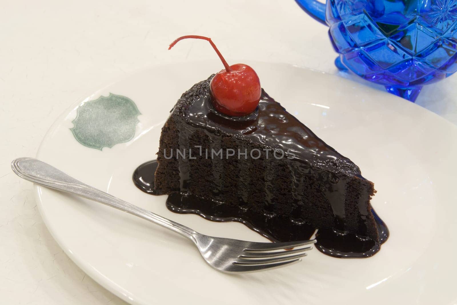 Chocolate cake decorated with red cherries on white plate.