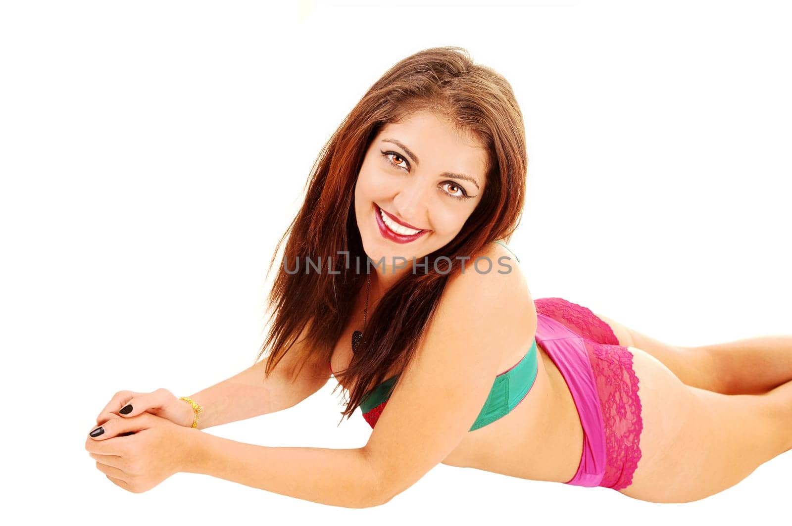 A beautiful young woman lying in pink lingerie on her stomach on the.floor for white background and smiling..