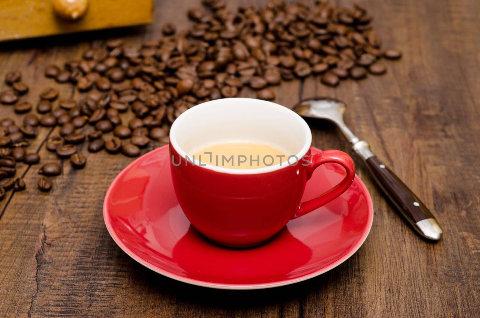Red cup of espresso and a spoon in front of beans and coffee grinder