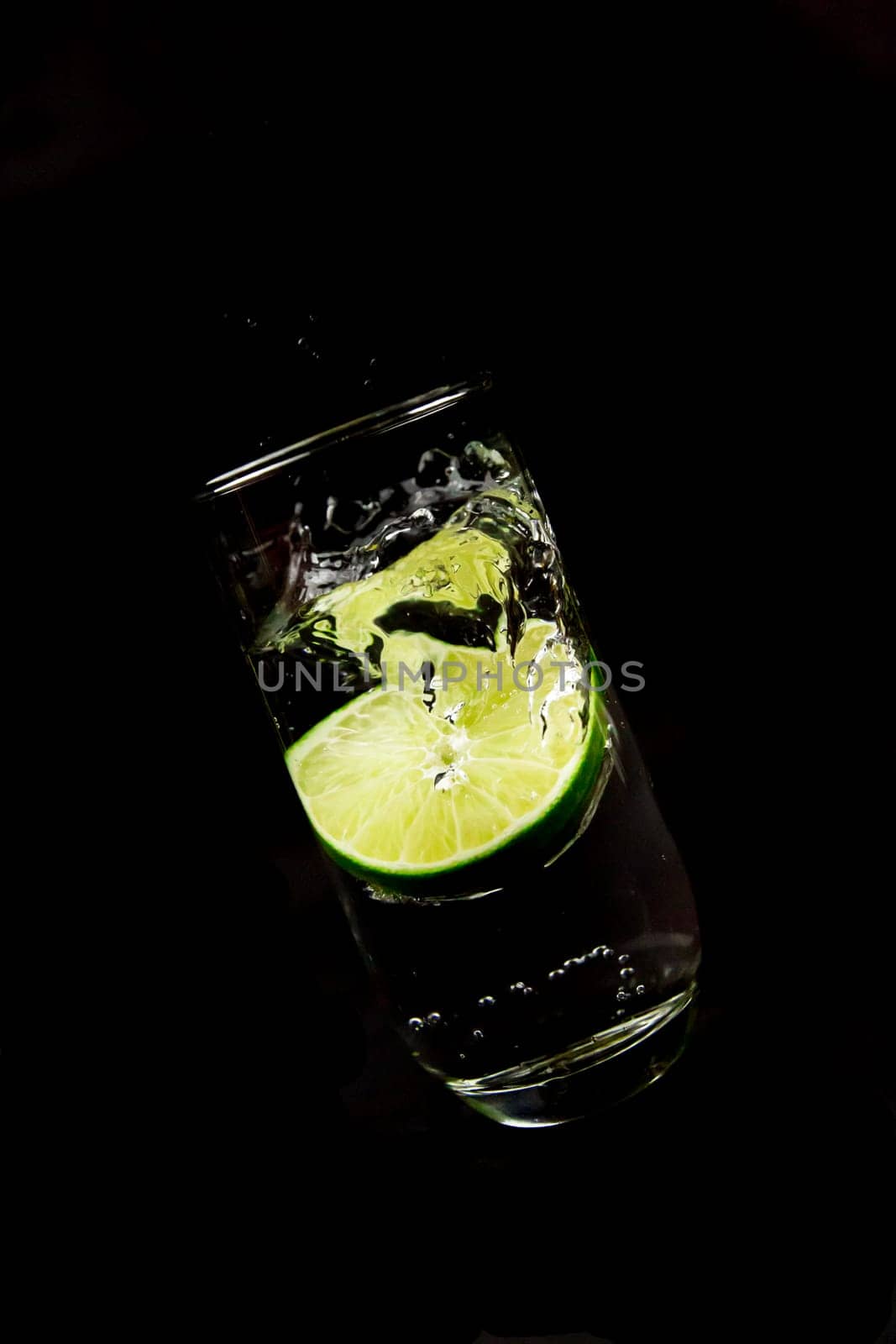 Lime falls into a glass of water against a black background