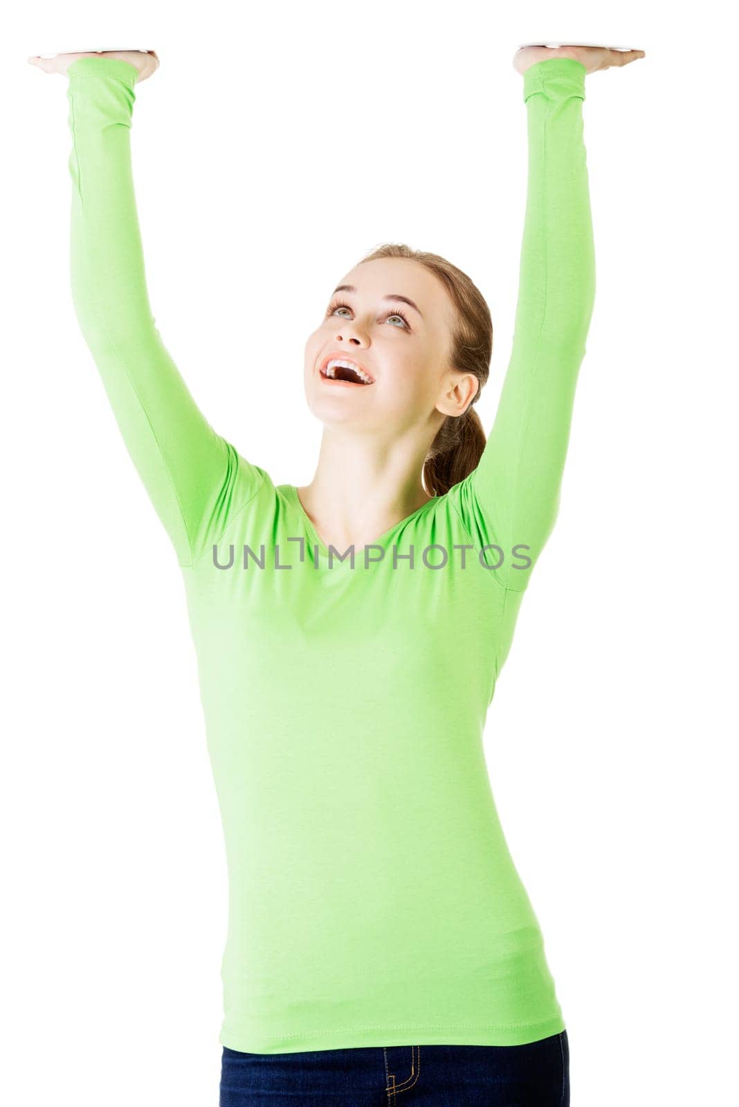 Smiling young woman is holding something abstract above her head. Happy girl with raised hands. Isolated on white background.