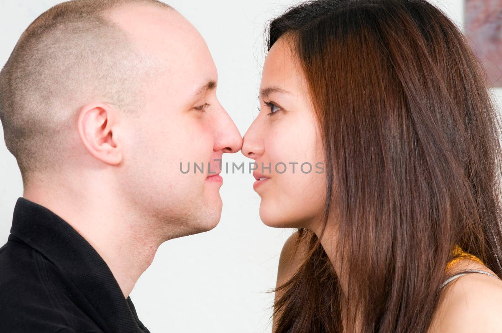 Head-and-shoulder shot in profile of a young couple nose to nose in front of a white background