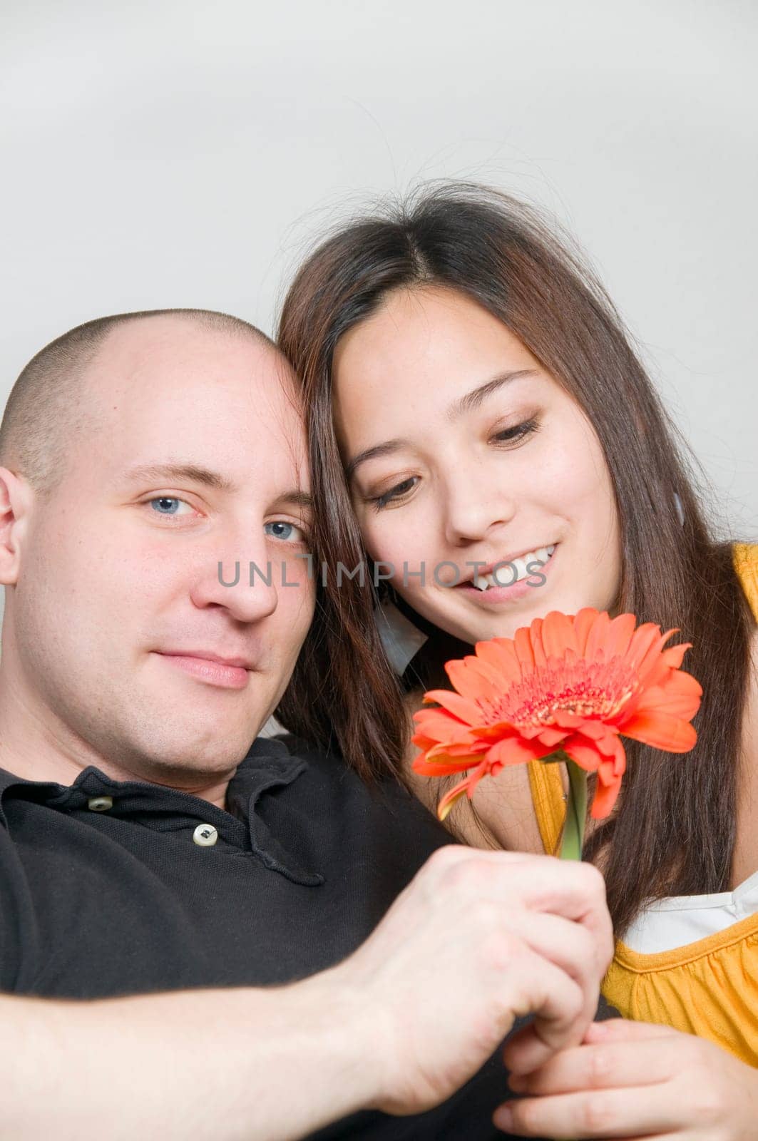 Upper body portrait of a young couple at home on the couch with flower in hand and amorous looks
