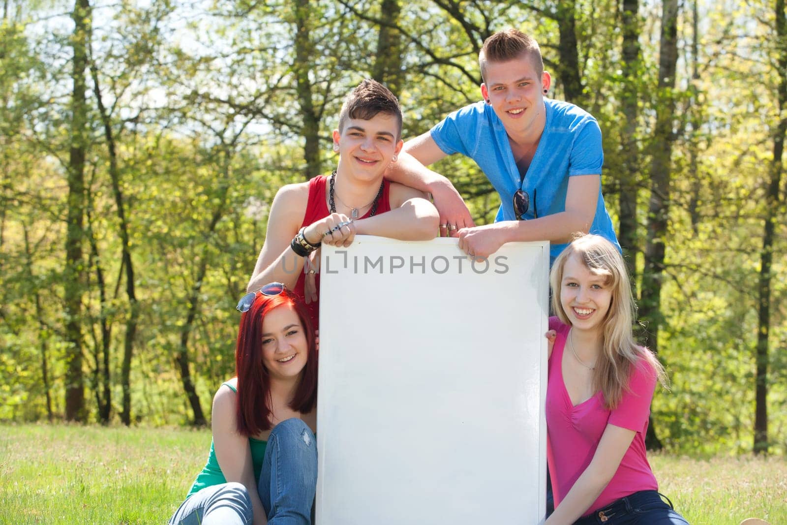 Four teenagers in colored shirts and a white board which can be used for your advertisements