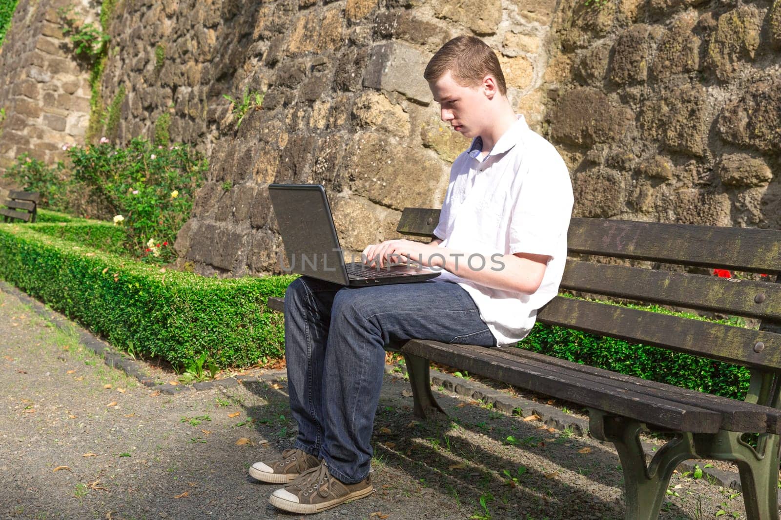 Young man sits on a bench and works with a laptop