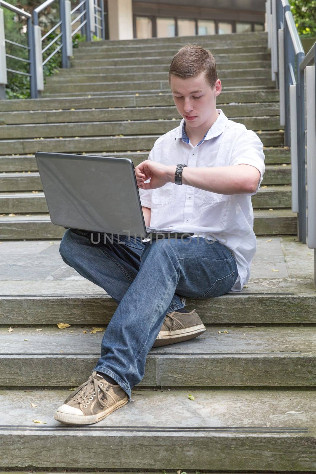Young man sits on stairs and works on his laptop