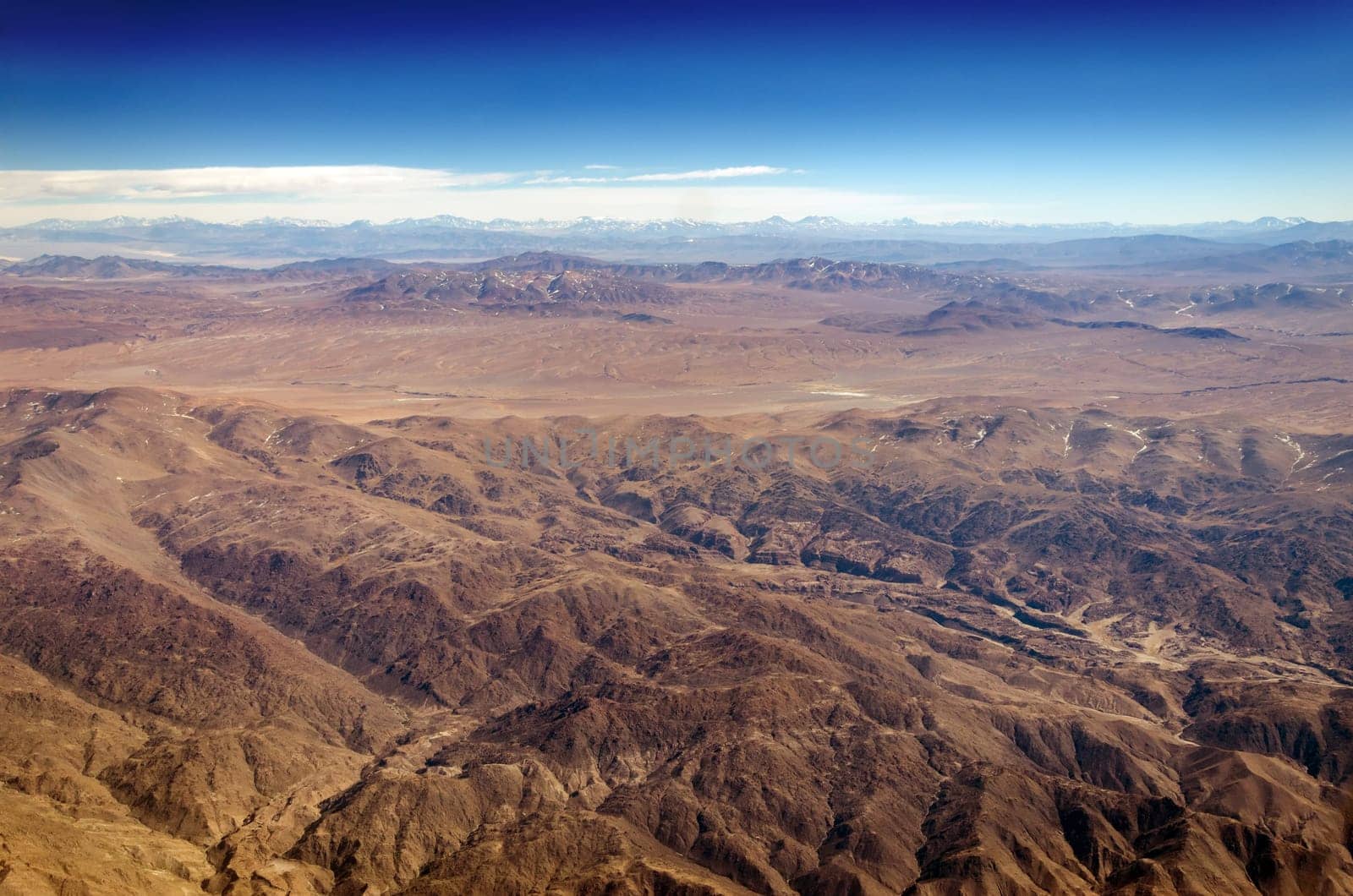Dry desert and hills with snow capped mountains in the background somewhere over South America