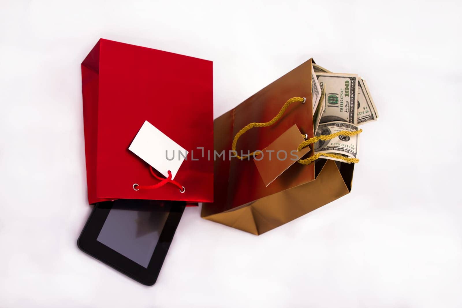 A red gift bag with a Tablet PC and a gold gift bag with dollars, isolated.