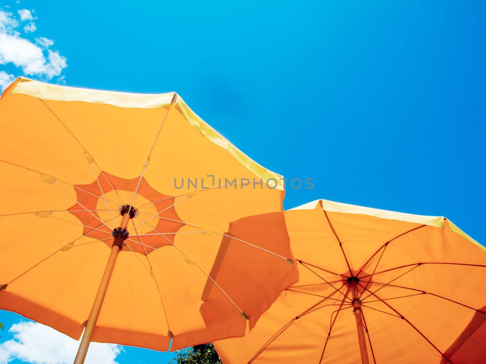 two umbrellas in orange from below against blue sky with small clouds