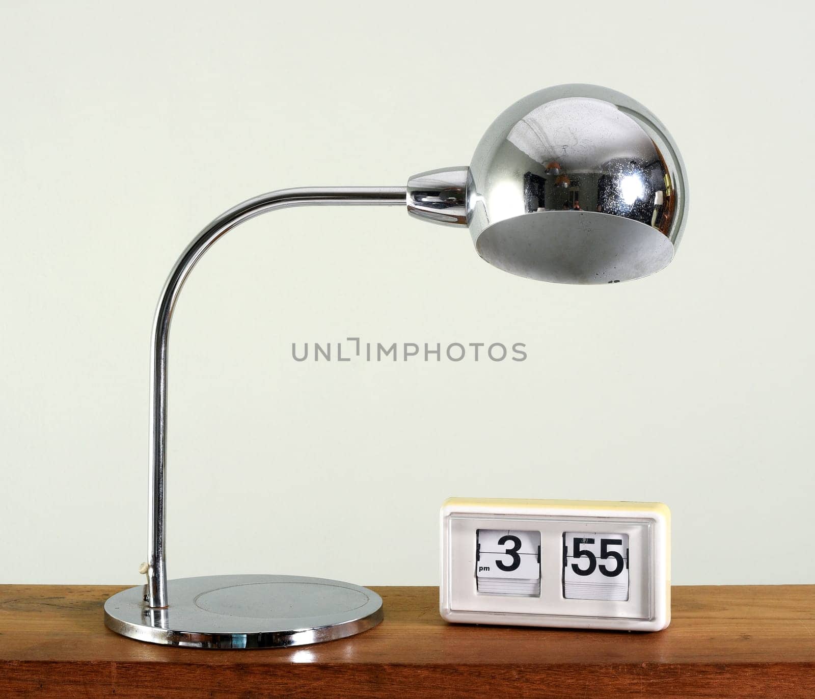 Stylish chrome table lamp with spherical shade and bent arm alongside an old clock on a wooden table