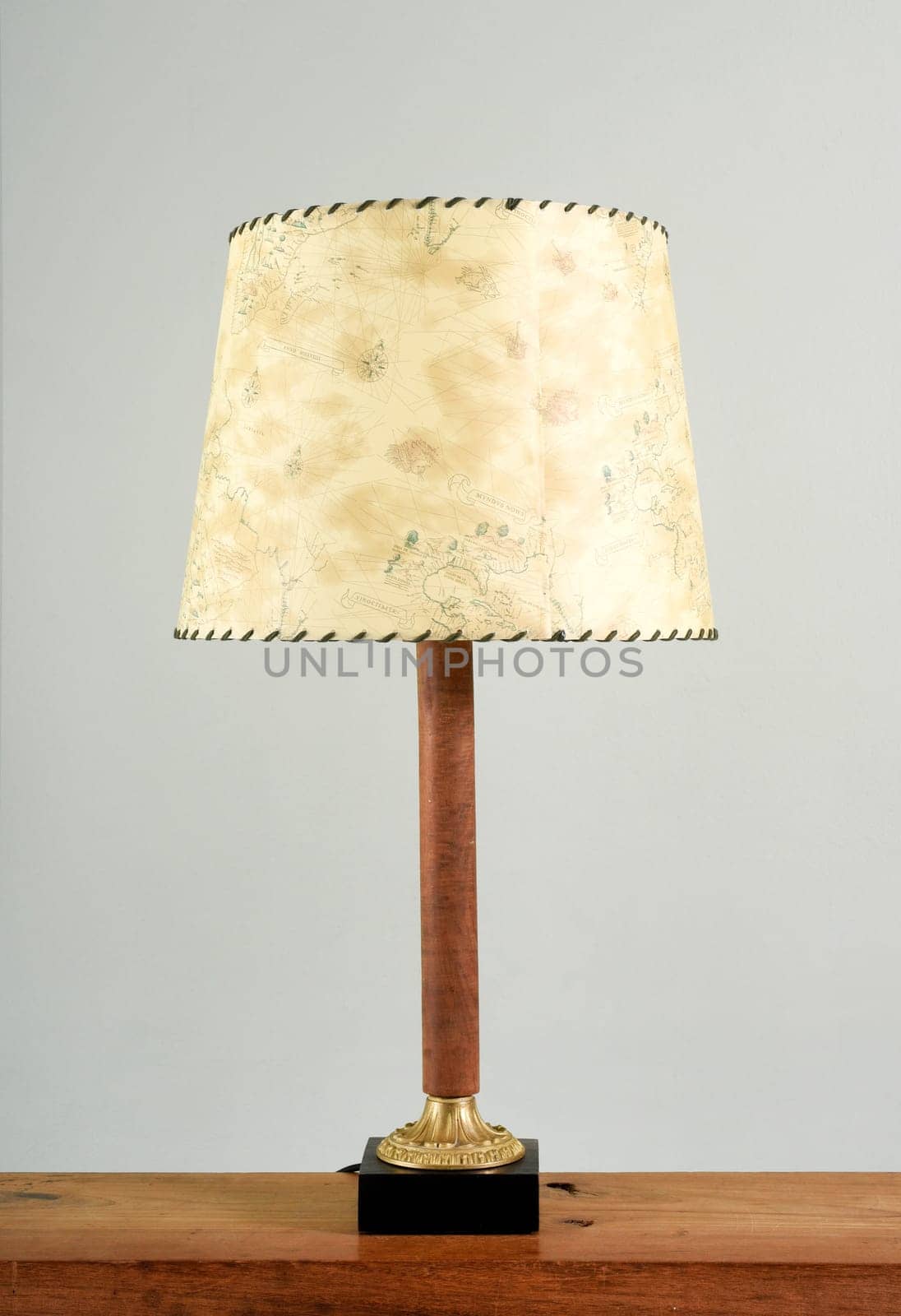 Classic table lamp with yellowish shade on wooden leg, close-up on the shelf against white background