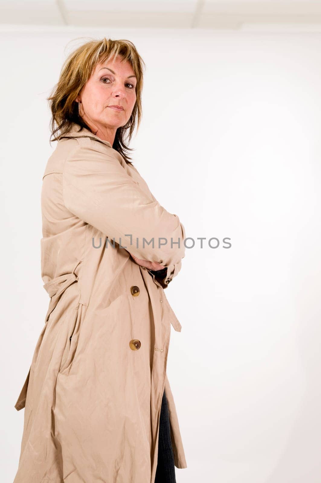 side three-quarter view of a middle-aged woman in front of a white background with folded arms arrogantly looking into the camera