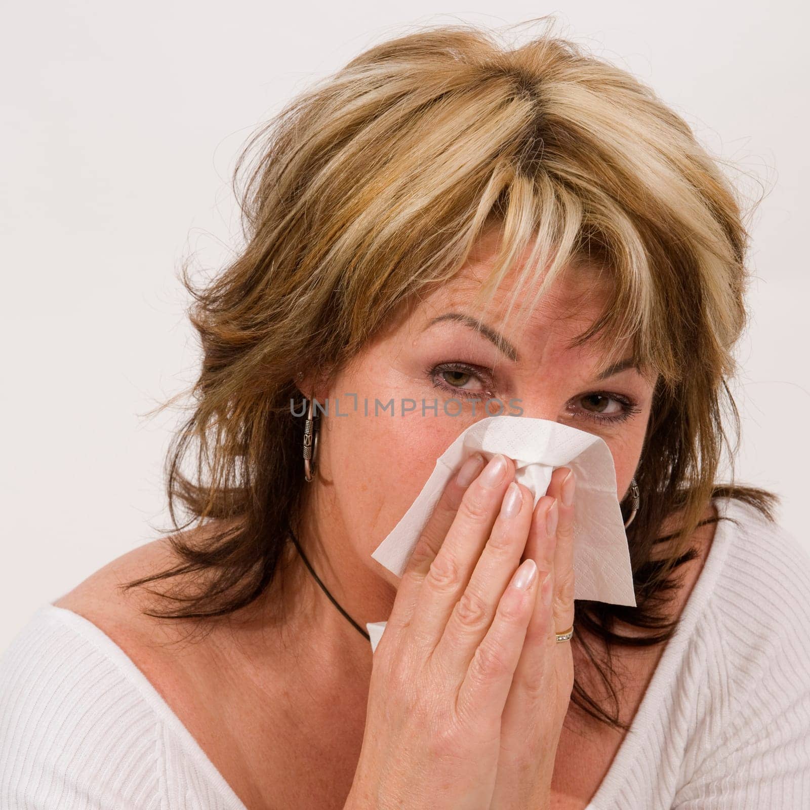 Head-and-shoulder shot of a middle-aged woman against a white background sniffing her nose