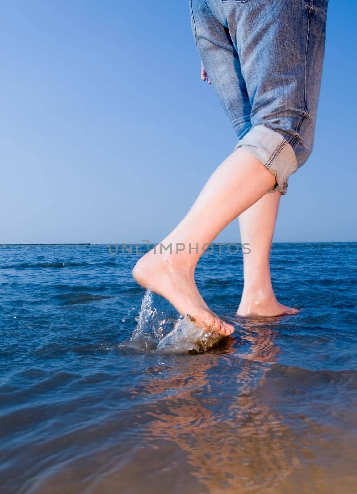 Leg view of a middle-aged woman with high-rolled jeans Barefoot on the beach in shallow water