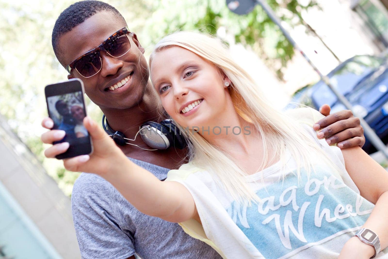 Young laughing multicultural couple take photo with smartphone mobile phone in summer