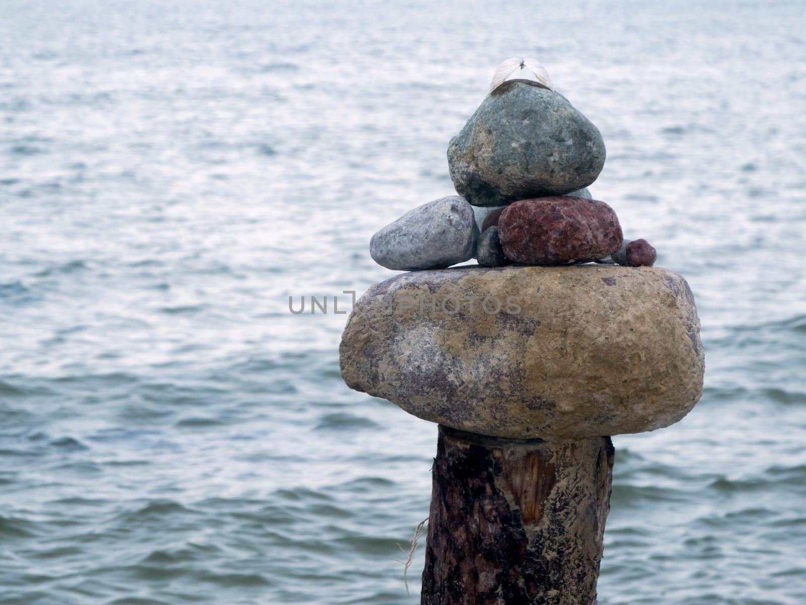 Natural stones stacked on top of each other on wooden posts in front of North Sea water surface