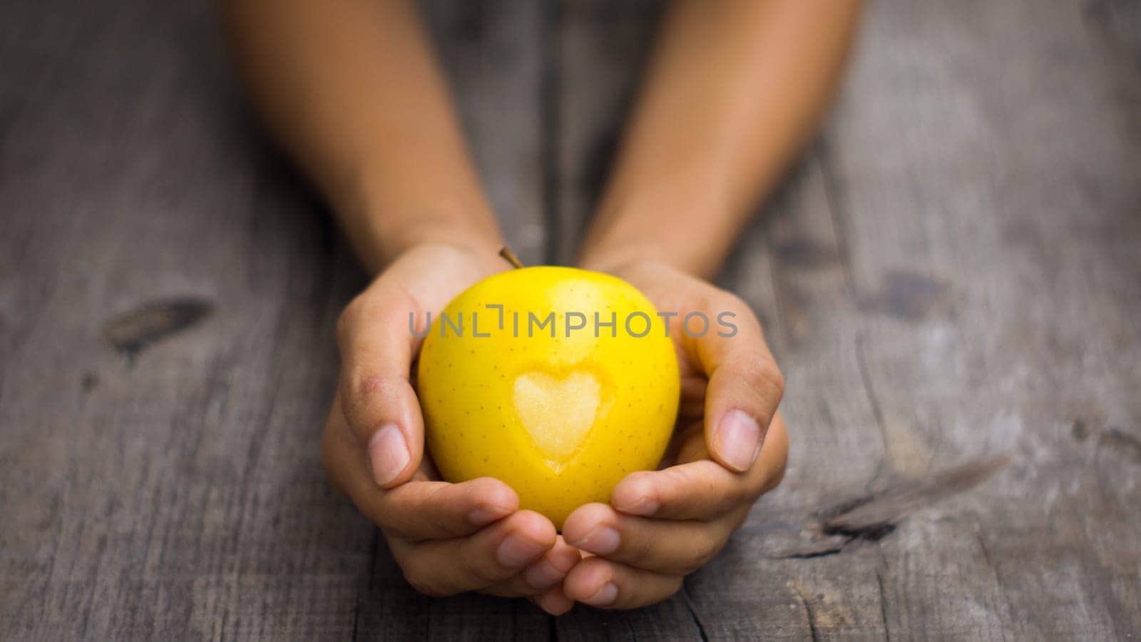 A person holding a Yellow Apple with engraved heart
