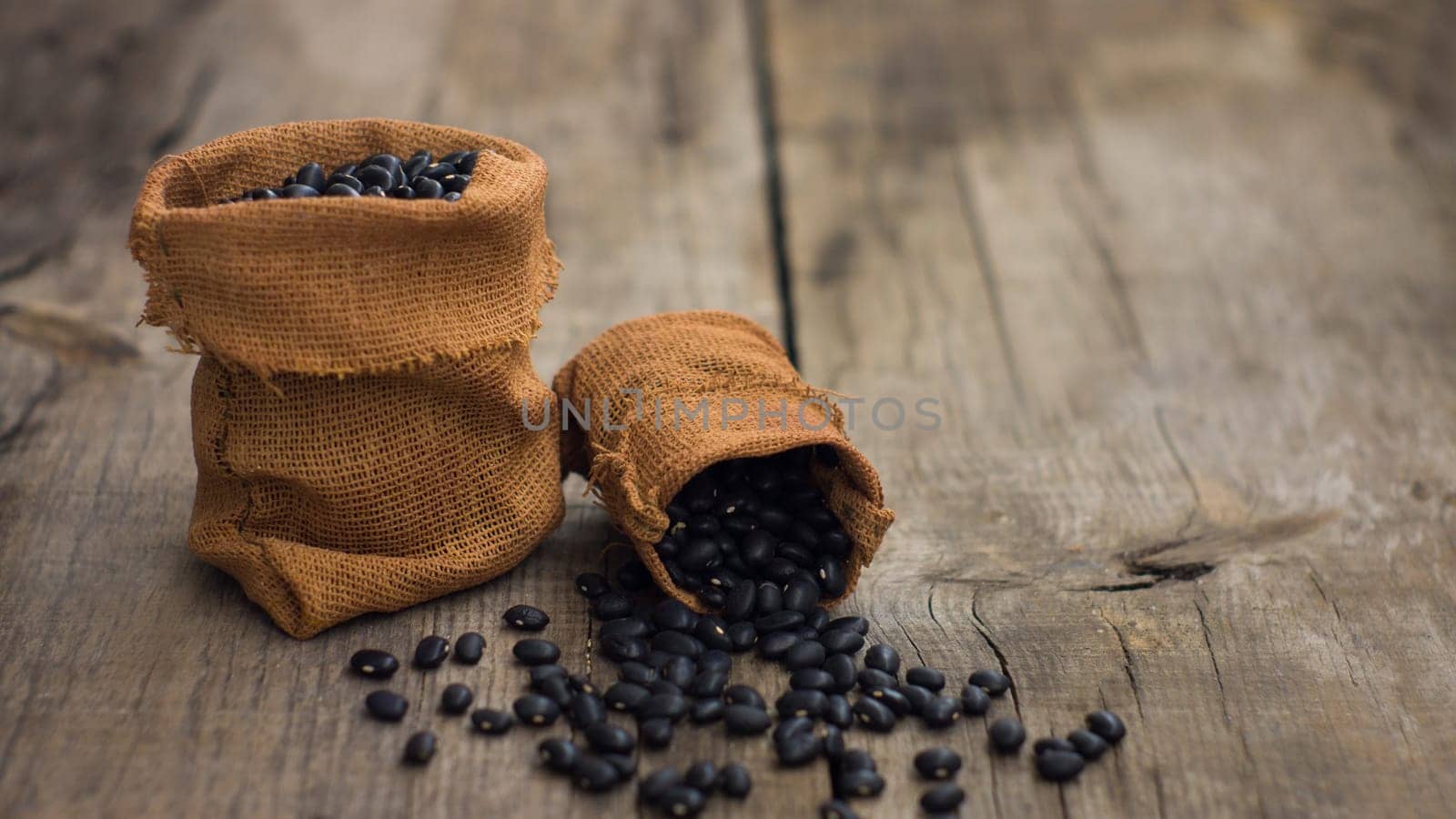 Small bags with black beans on wooden background